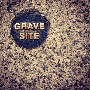 A coin-sized marker in concrete that says 'Grave Site'